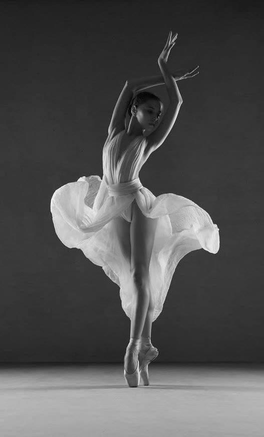 Danseuse classique sur pointes en robe blanche fluide, bras levés, photographie en noir et blanc