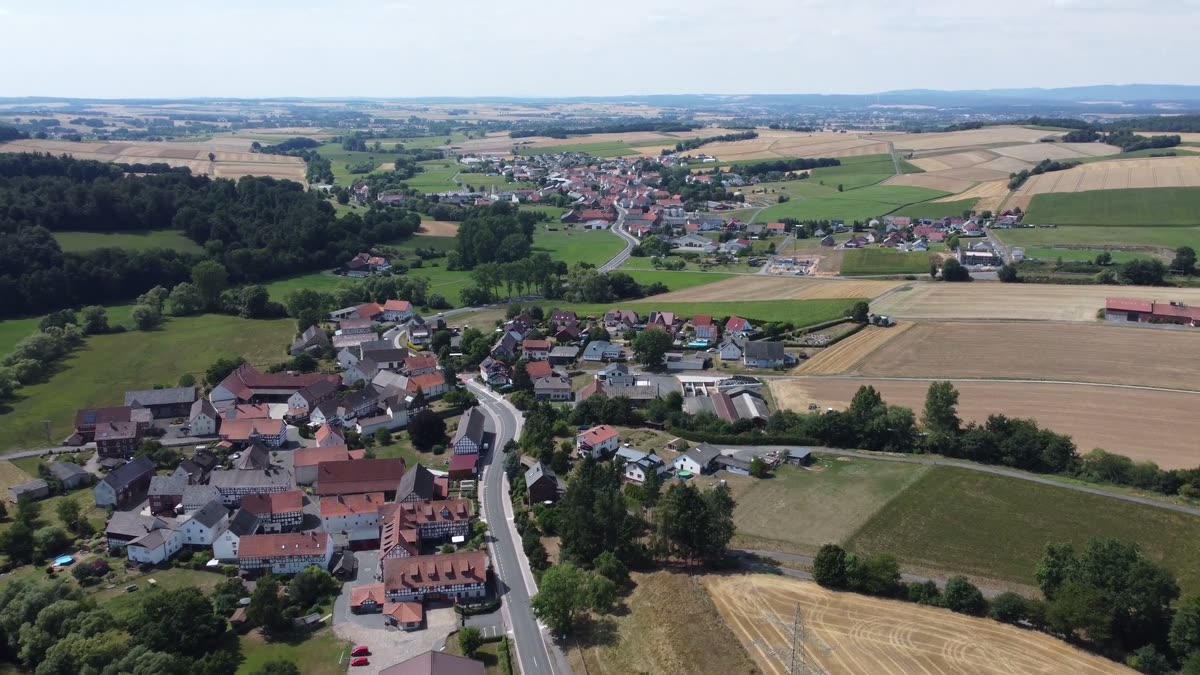 Vue aérienne d’un village aux toits rouges entouré de champs dorés et de forêts