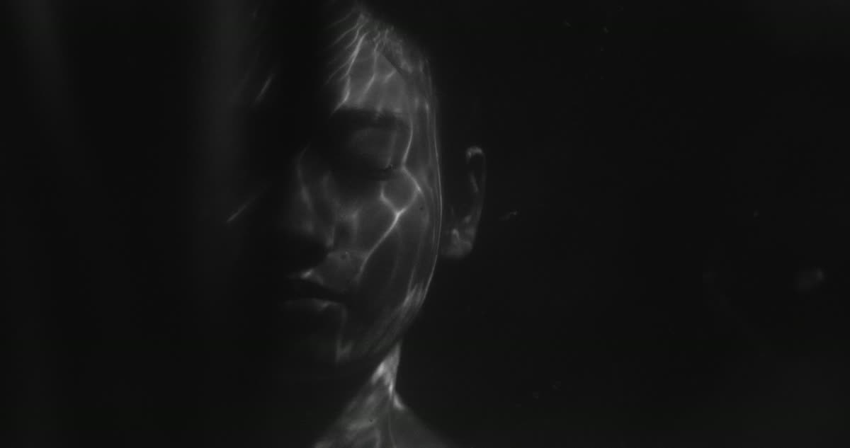 Visage de femme aux yeux clos dans l’obscurité, strié de reflets lumineux de l’eau