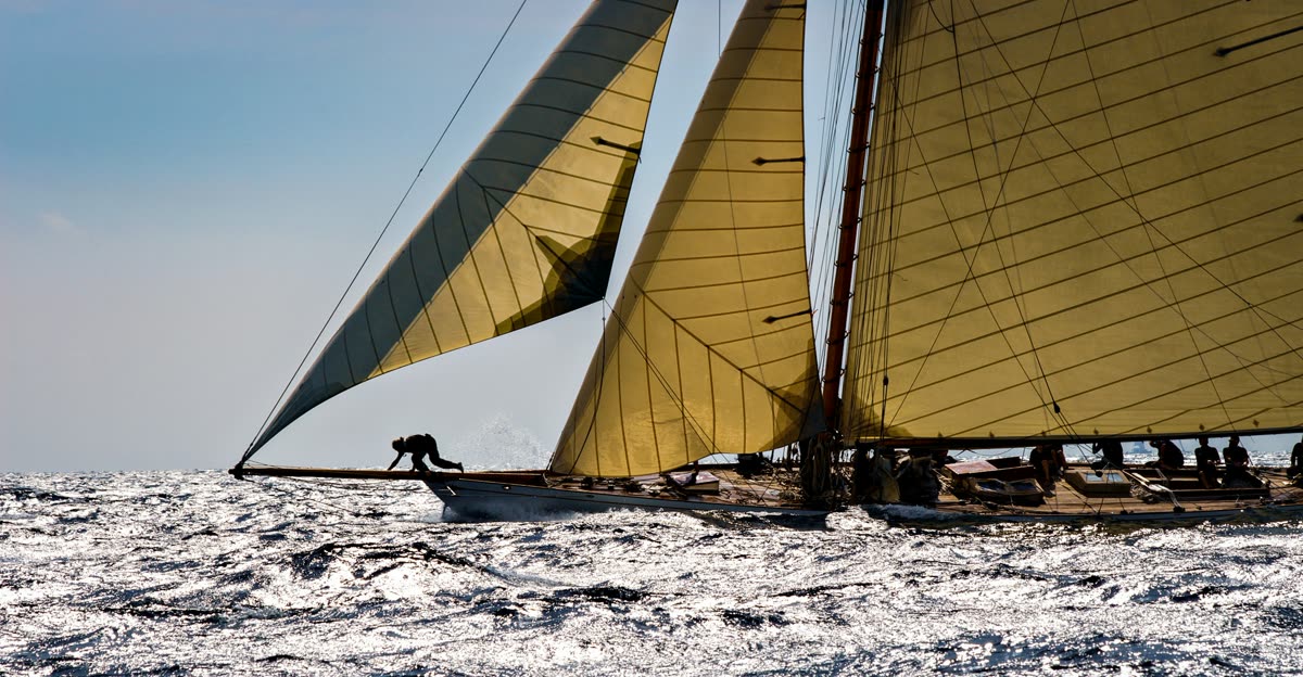 Voilier classique toutes voiles dehors sur une mer scintillante, équipier à l’avant du beaupré