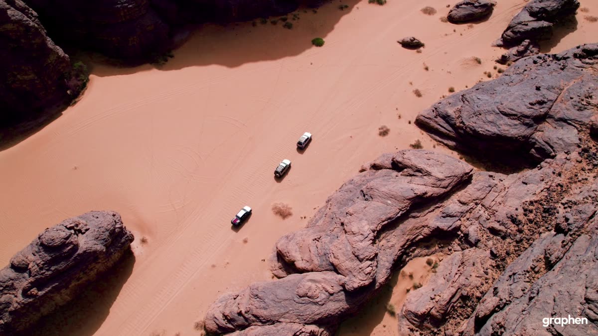 Vue aérienne de trois 4x4 blancs roulant sur le sable rose d’un canyon rocheux