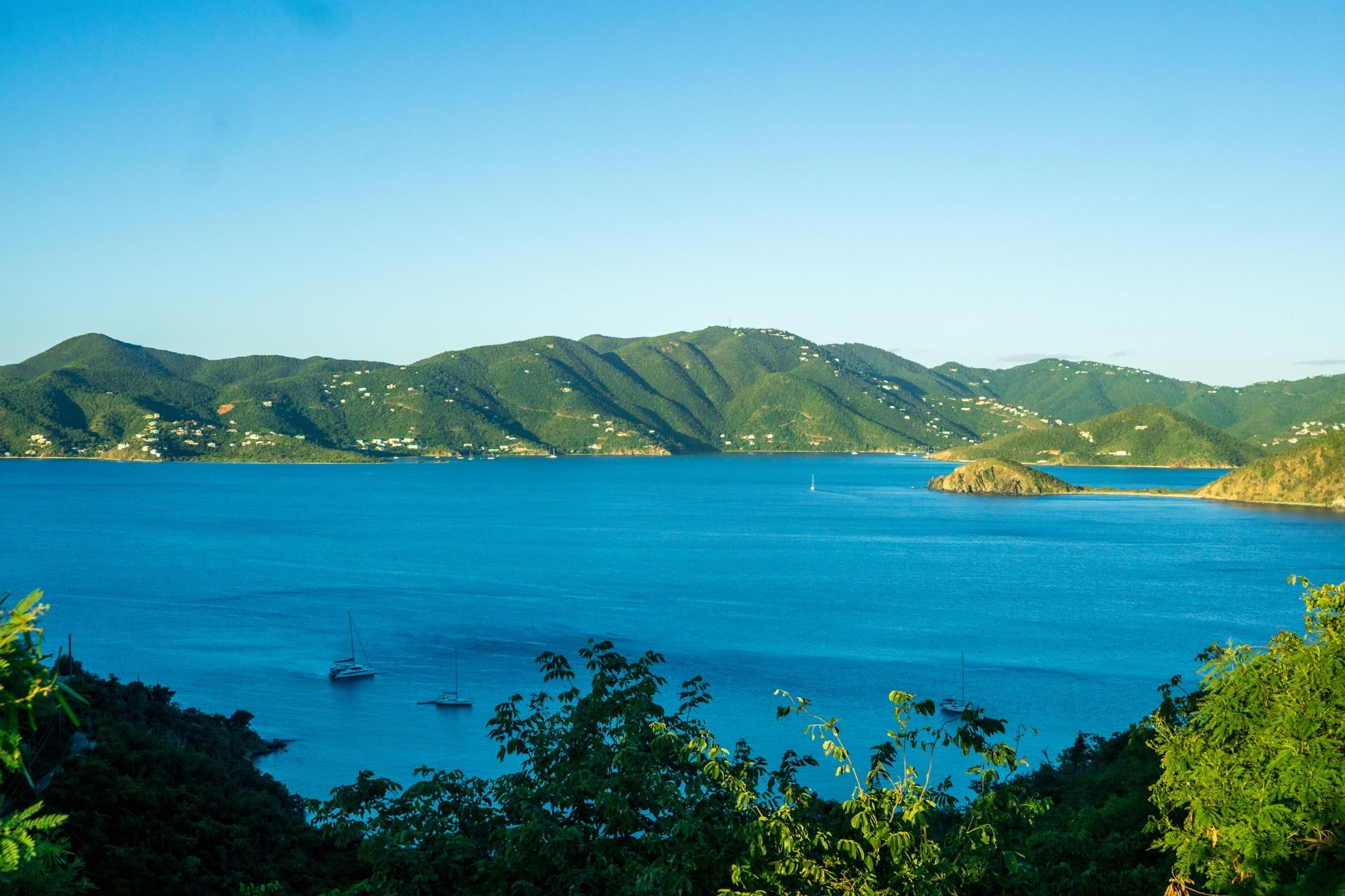 Turquoise Caribbean bay, yachts at anchor against lush green hills
