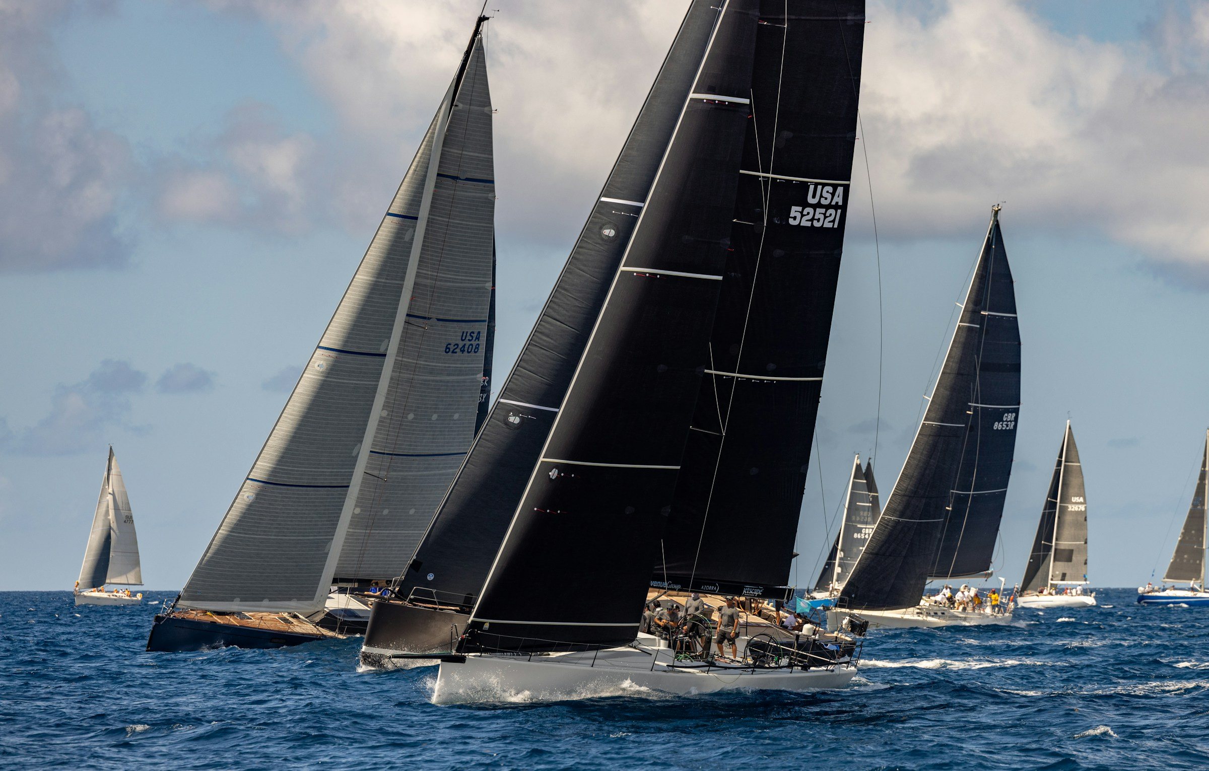 Flotte de voiliers de course aux voiles noires, au près sur une mer bleu profond