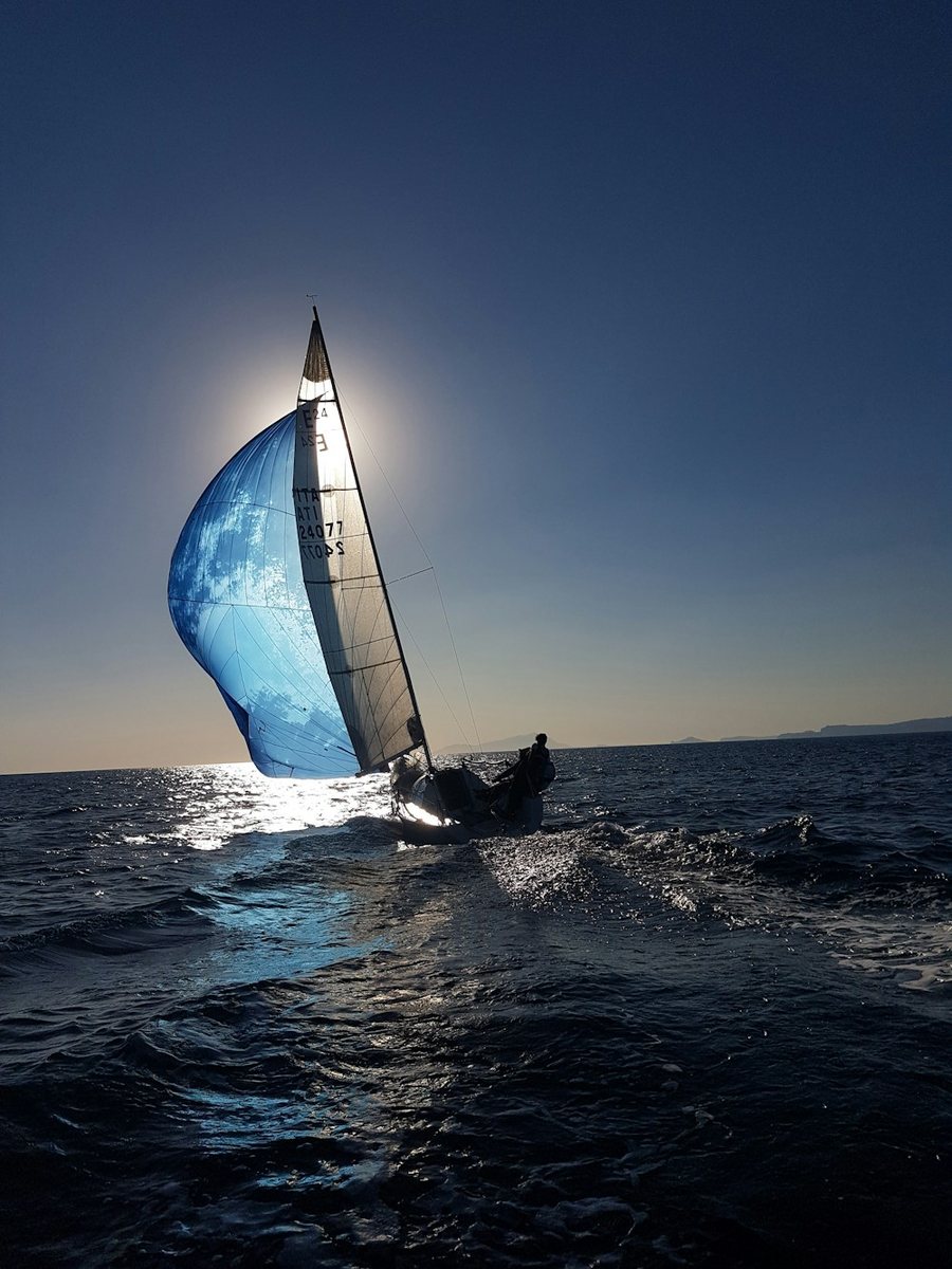 Yacht under blue spinnaker, backlit against dark waters