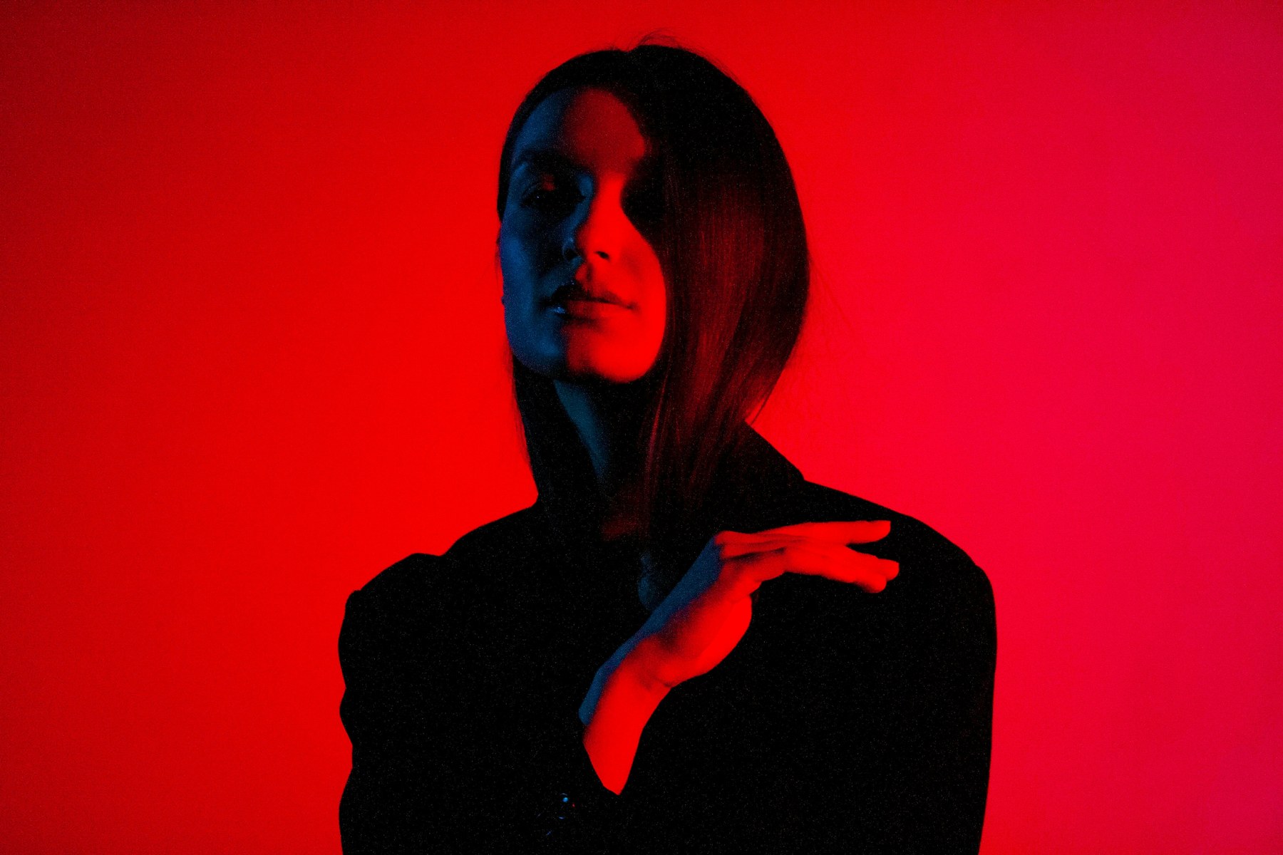 Portrait de femme en veste noire, éclairée de rouge et de bleu devant un fond rouge