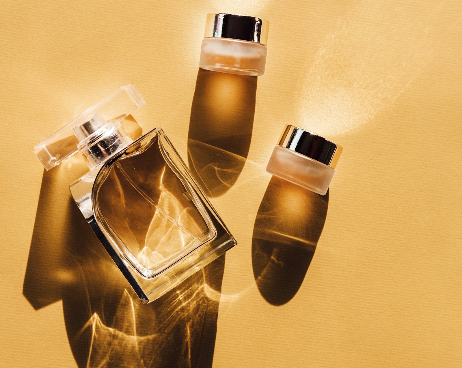 Flacons de parfum et pots de crème dorés projetant leurs ombres sur un fond ocre, réalisation Studio 47