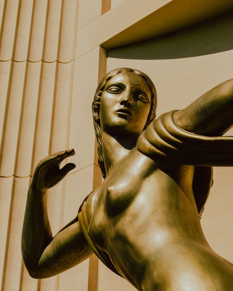 Statue art déco en bronze devant une façade cannelée, lumière dorée, page réalisateur de Studio 47